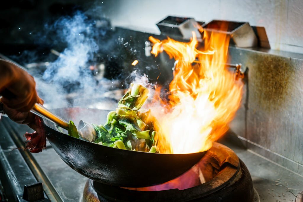 Chef in restaurant kitchen at stove with high burning flames